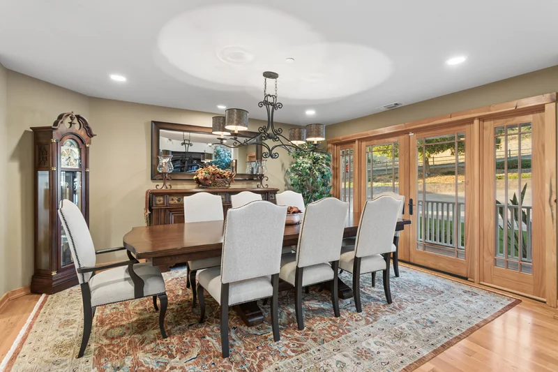 Dining area with white upholstered chairs beside broad windows.