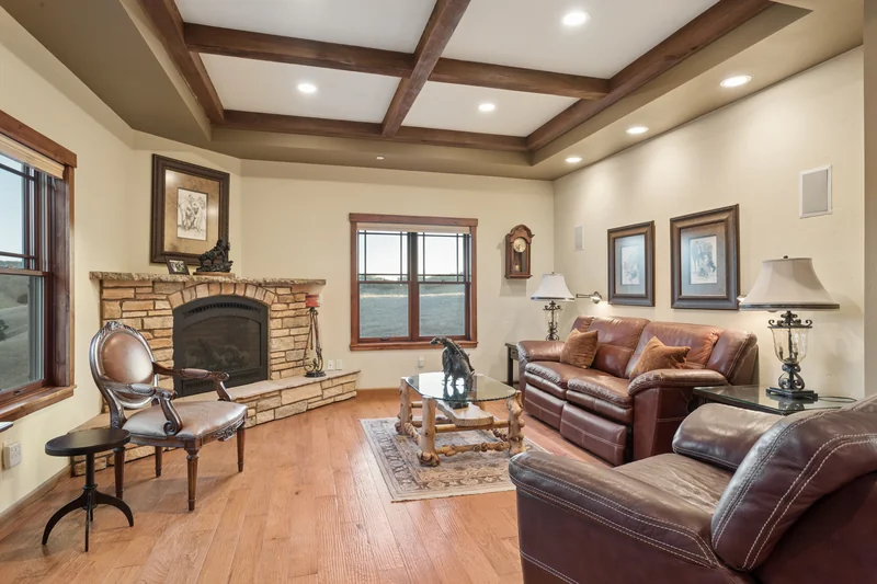 Living area beneath exposed beams beside a stone fireplace.