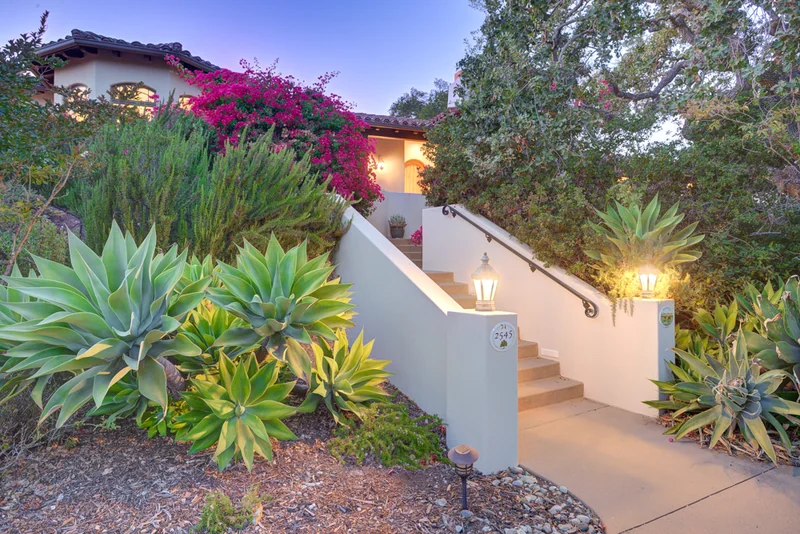 Garden steps leading to a home among flowering shrubs at dusk.