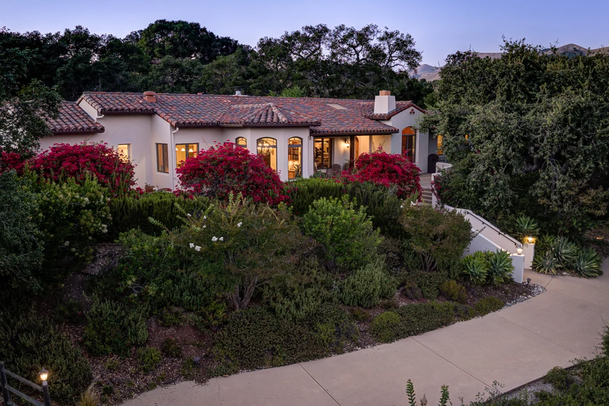 Twilight aerial of a red-roofed home surrounded by mature trees.