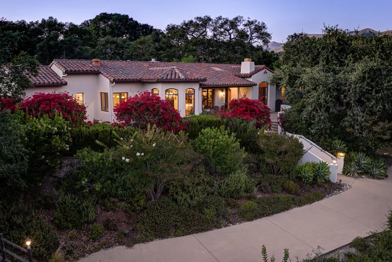 Twilight aerial of a red-roofed home surrounded by mature trees.