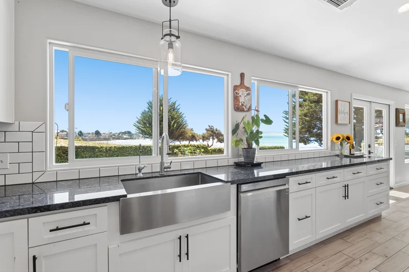 Kitchen sink and white cabinetry beneath a garden-facing window.