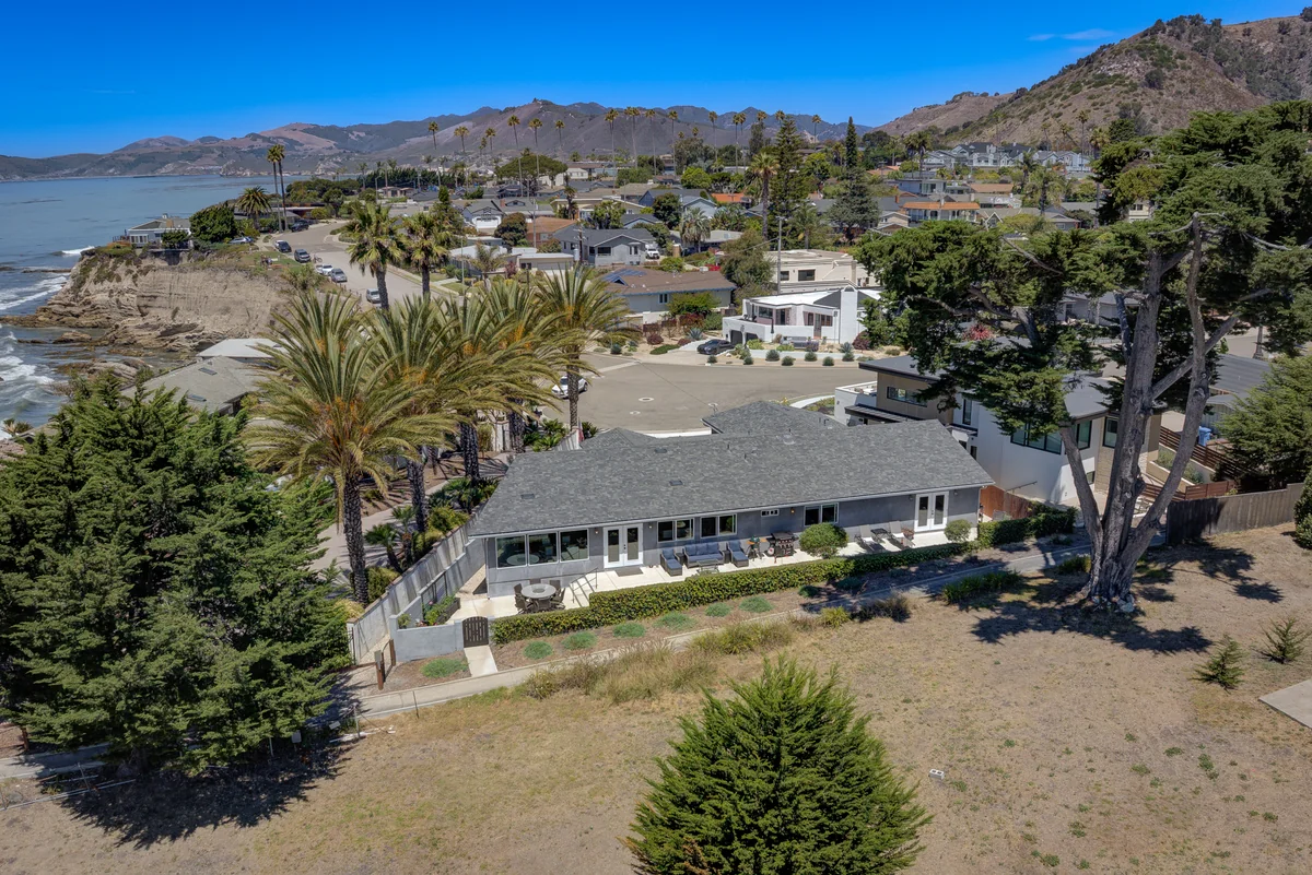 Coastal home with palms, a bluff-top garden and hills beyond.
