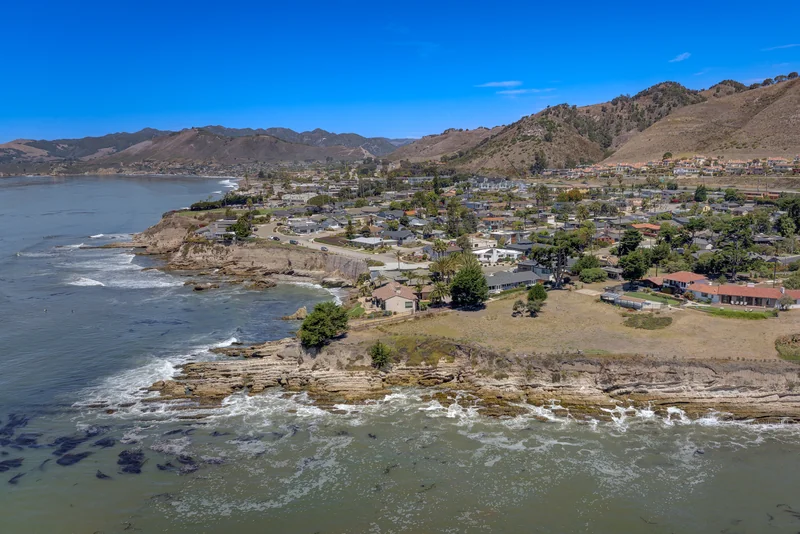 Rocky coastline with bluff-top homes and hills in the distance.