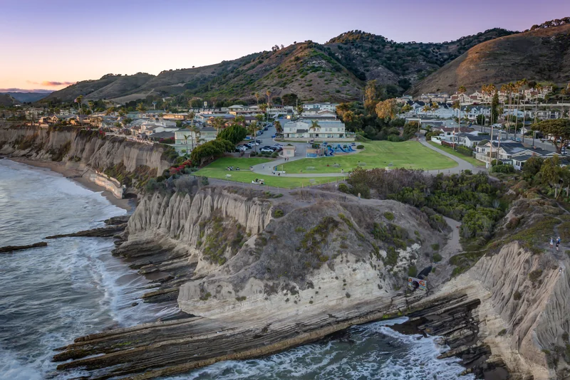 Coastal home above rocky cliffs with hills beyond at dusk.