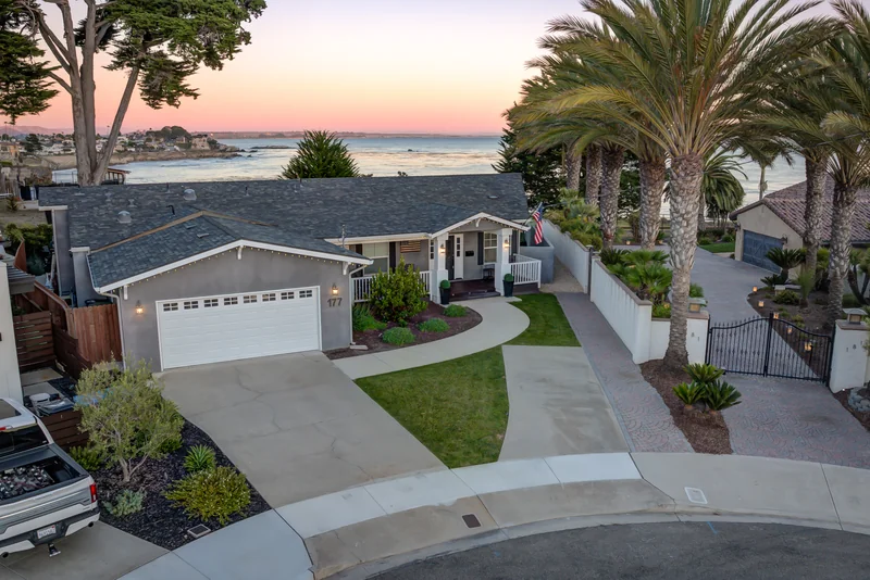 Elevated front view of a palm-lined home with sunset over the ocean.