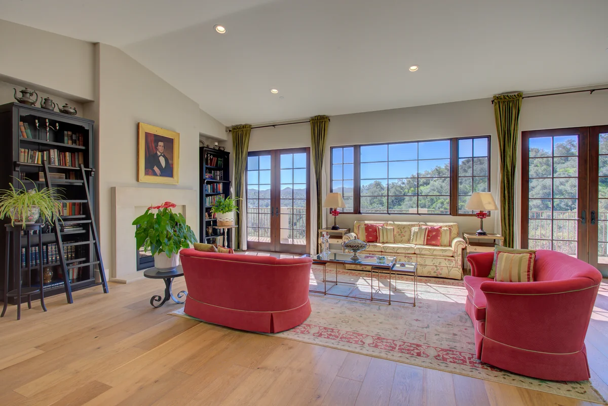 Living room with red armchairs and tall windows overlooking the hills.
