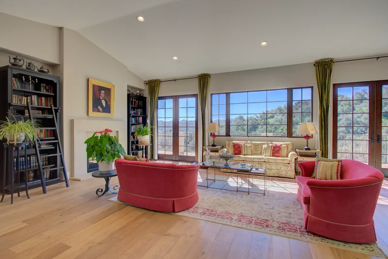 Living room with red armchairs and tall windows overlooking the hills.