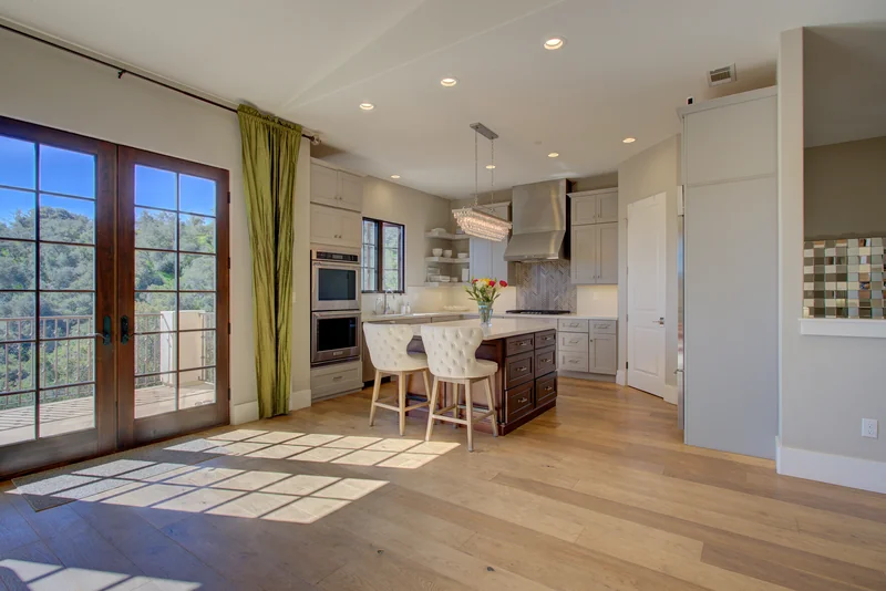 Breakfast table beside tall windows and a bright kitchen.