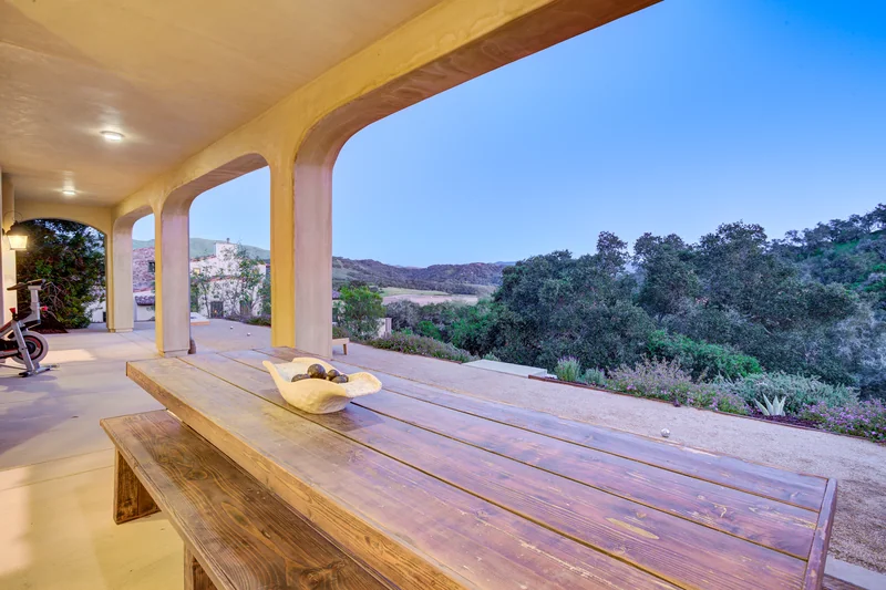 Covered dining terrace overlooking green hills in evening light.