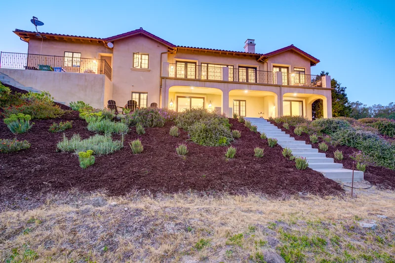 Illuminated two-story rear facade above a landscaped slope.